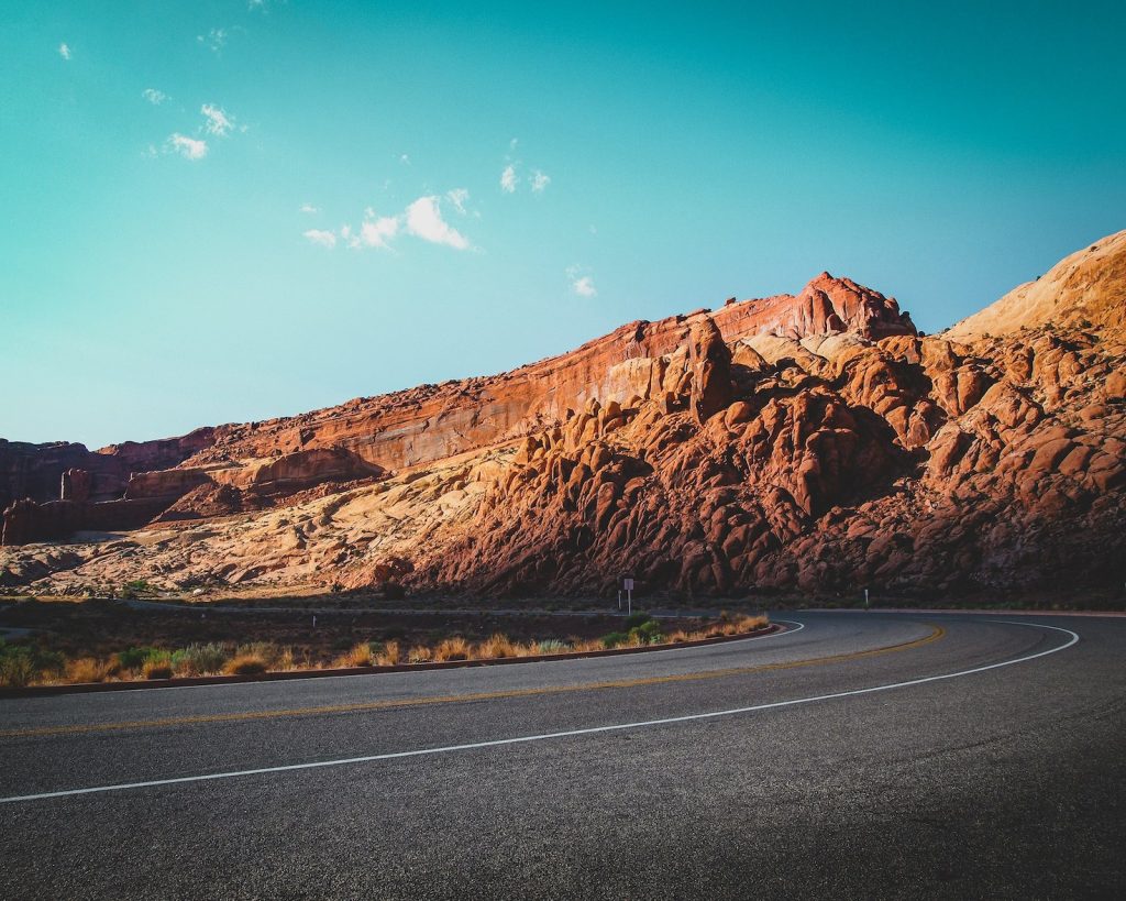 Photo of an empty road with a mountain in the foreground and blue sky.